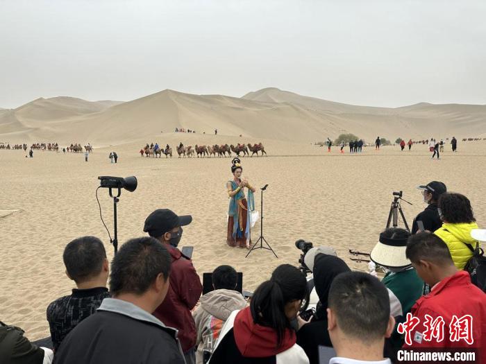 圖為2023年4月底，敦煌大漠“逐舞者”奧楠在鳴沙山月牙泉景區(qū)視頻直播，吸引游人圍觀?！●T志軍 攝